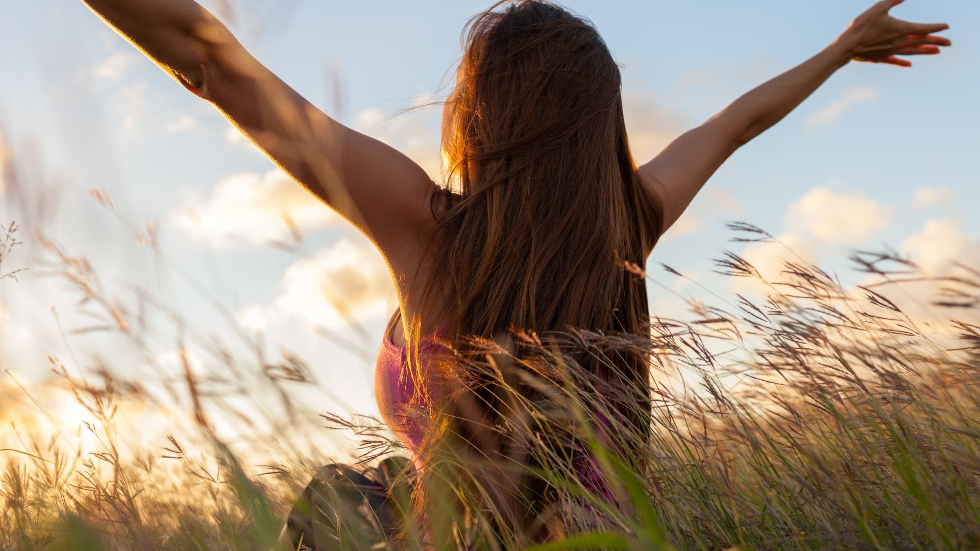 Femme bras ouverts dans un champ, au coucher du soleil